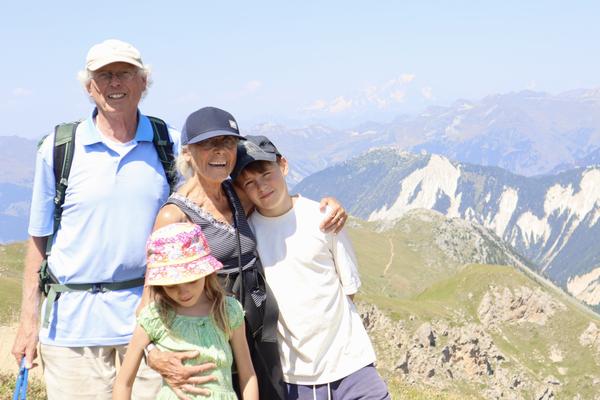 A family of four, including two adults and two children, poses for a photo on a sunny mountain top